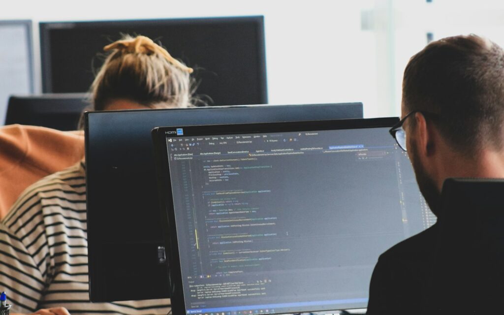 Zwei Entwickler arbeiten an Code auf Monitoren: Inhouse-Entwicklung im eigenen Team