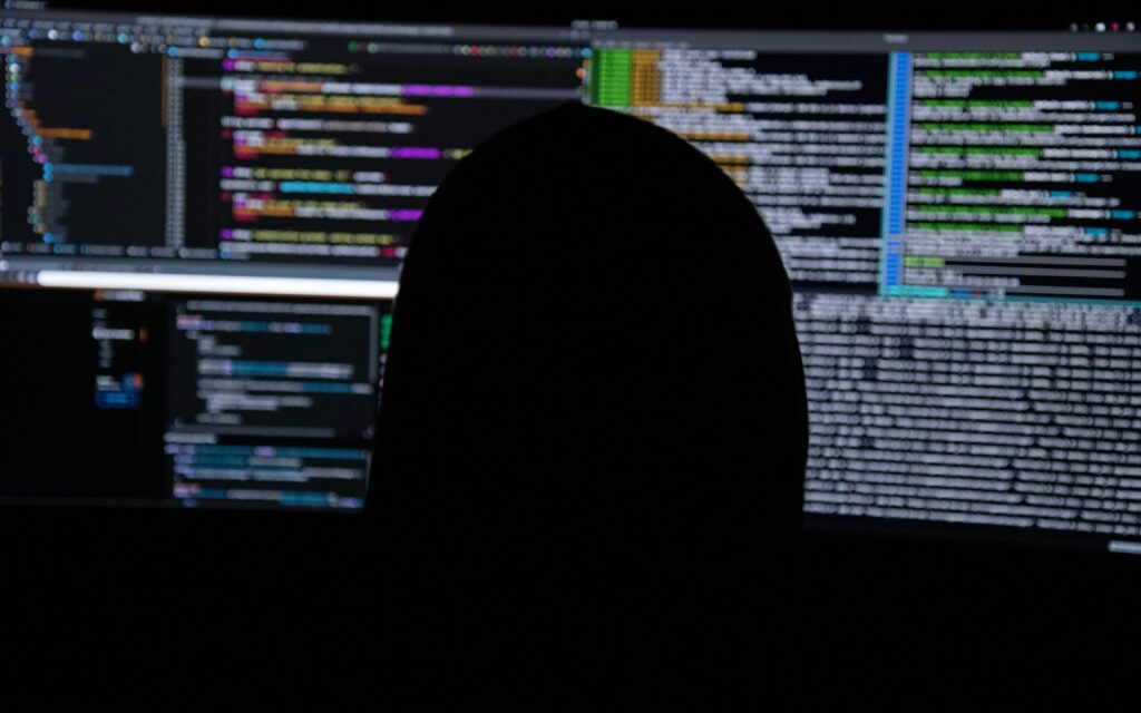 Person vor mehreren Monitoren mit Code: Cybersecurity für KMU braucht Überwachung und klare Prozesse