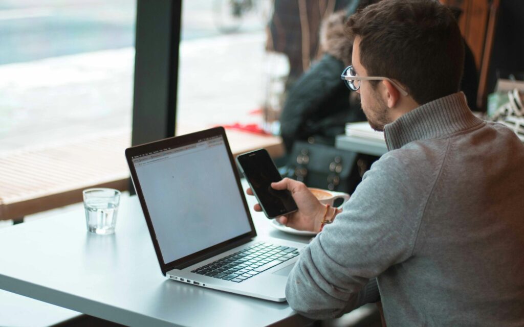 Mitarbeiter mit Laptop und Smartphone am Fenster, Symbolbild zu eSIM Firmenhandy