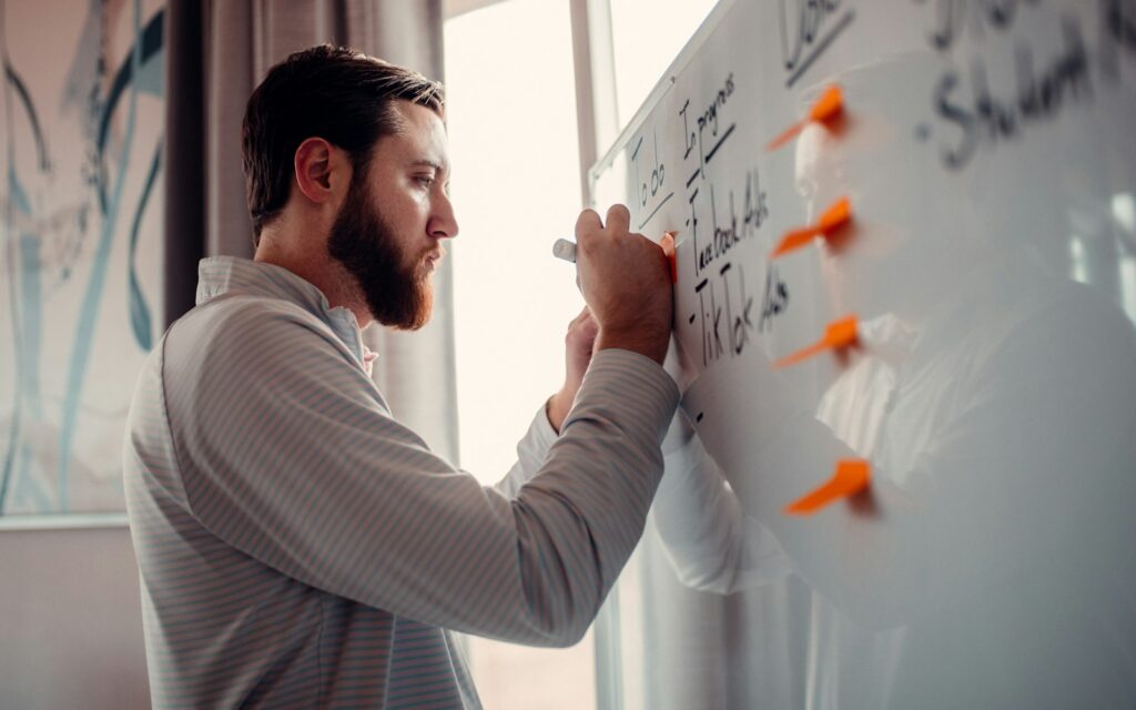 Mann schreibt Pläne an ein Whiteboard, Symbolbild zu Revenue Operations